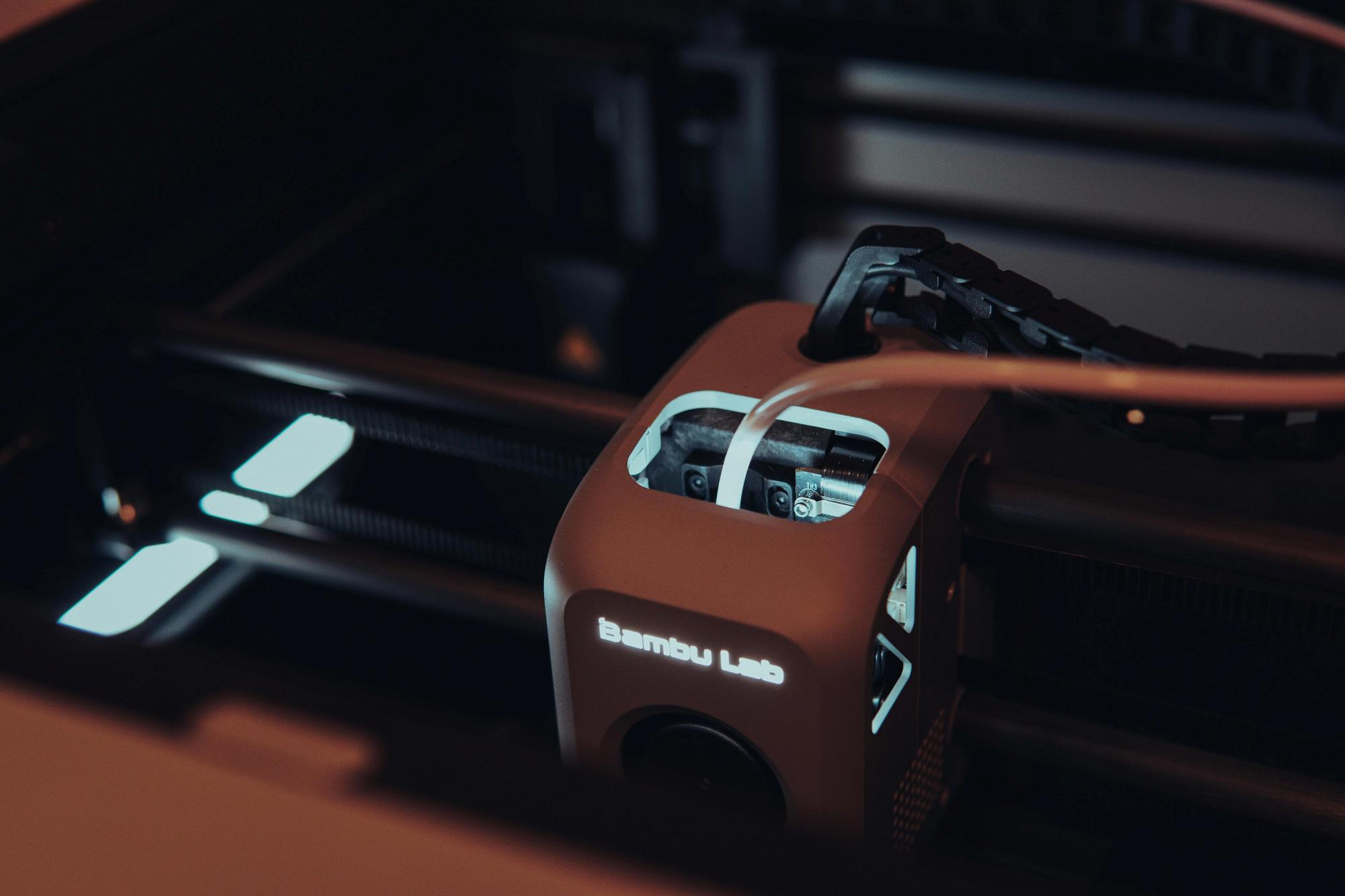 Close-up of a Bambu Labs 3D printer extruder and hotend with the logo illuminated.